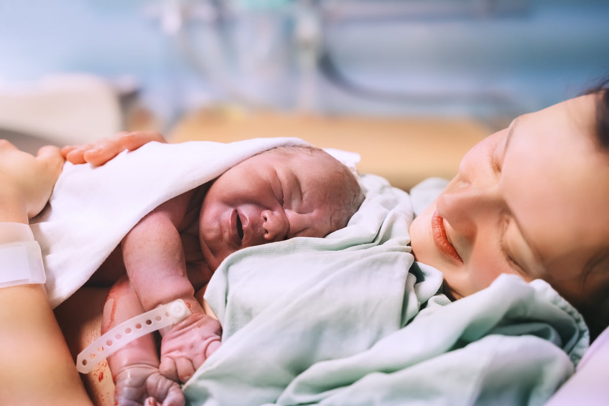 Mother and newborn. Child birth in maternity hospital. Young mom hugging her newborn baby after delivery. Woman giving birth.